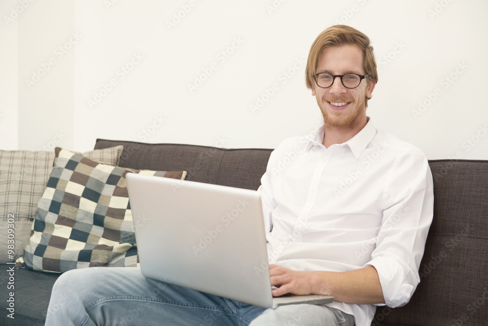 young man sitting on couch with laptop and smiles young man sitting on couch with laptop and smiles