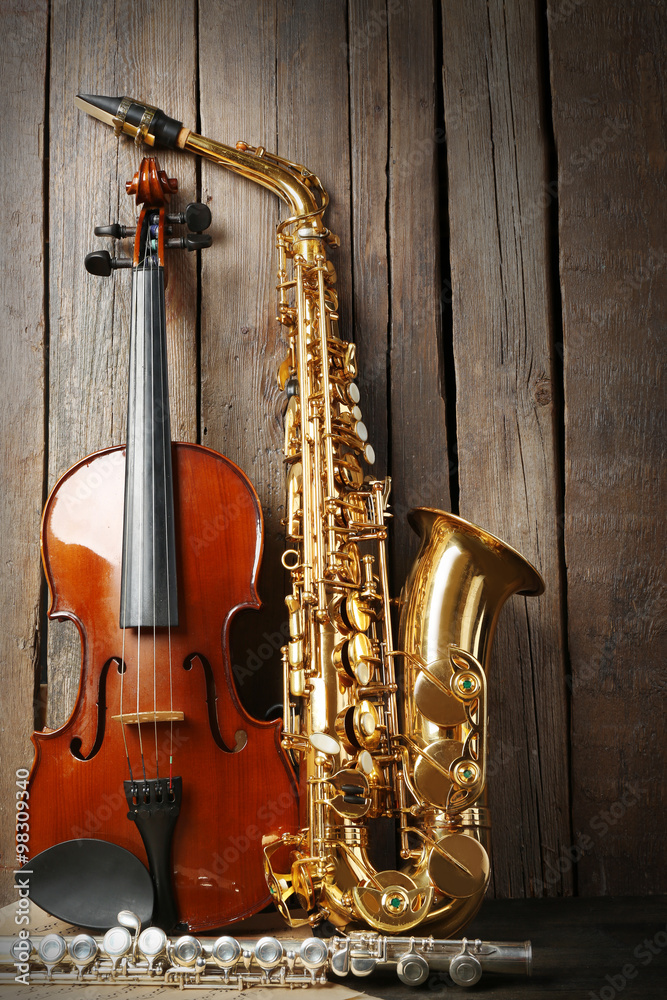 Naklejka premium Musical instruments: saxophone, violin and flute with notes on wooden background