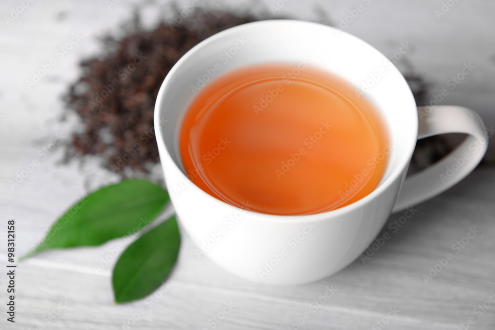Ceramic cup of tea with scattered tea leaves around on light wooden background