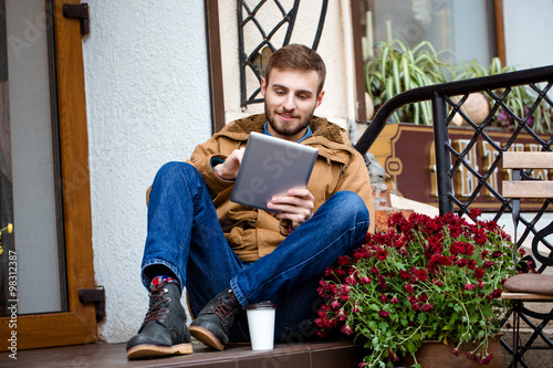 Smiling bearded man sitting on porch near entrance using tablet