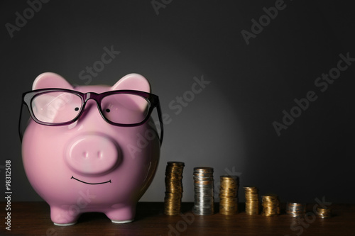 Piggy bank with glasses and coins on table, gray background