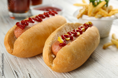 Delicious hot-dog with French fries and vegetables on white wooden table