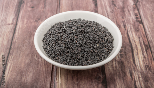 Black sesame seed in white bowl over wooden background