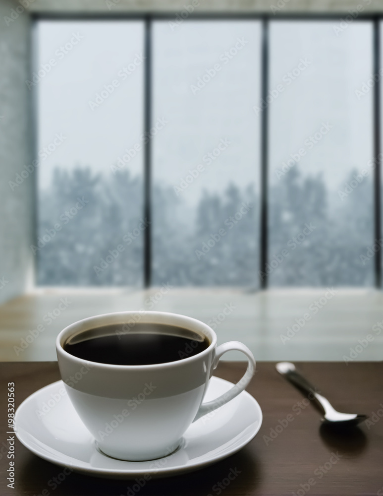 A cup of coffee and snowstorm view from large window on the background A cup of coffee and snowstorm view from large window on the background