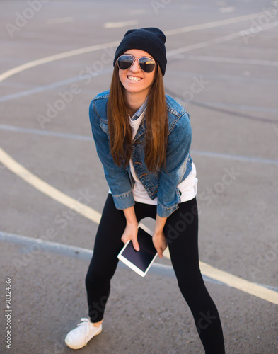 Female teen sits iasphalt road in urban wear and hat photo