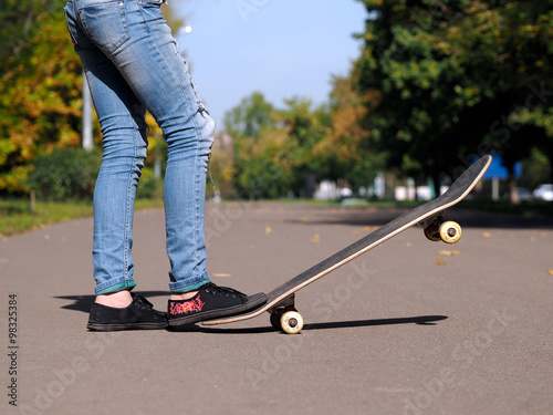 Ноги в кедах на скейтборде. Парк, лето. Джинсы рваные. Дорога