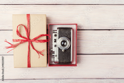 Gift box with retro camera over light wooden background