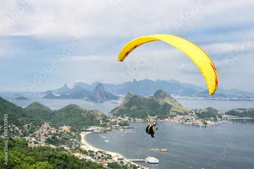 Bright yellow hang glider flying over the mountainous skyline of the city skyline from the Parque da Cidade park in Niteroi, Rio de Janeiro, Brazil 