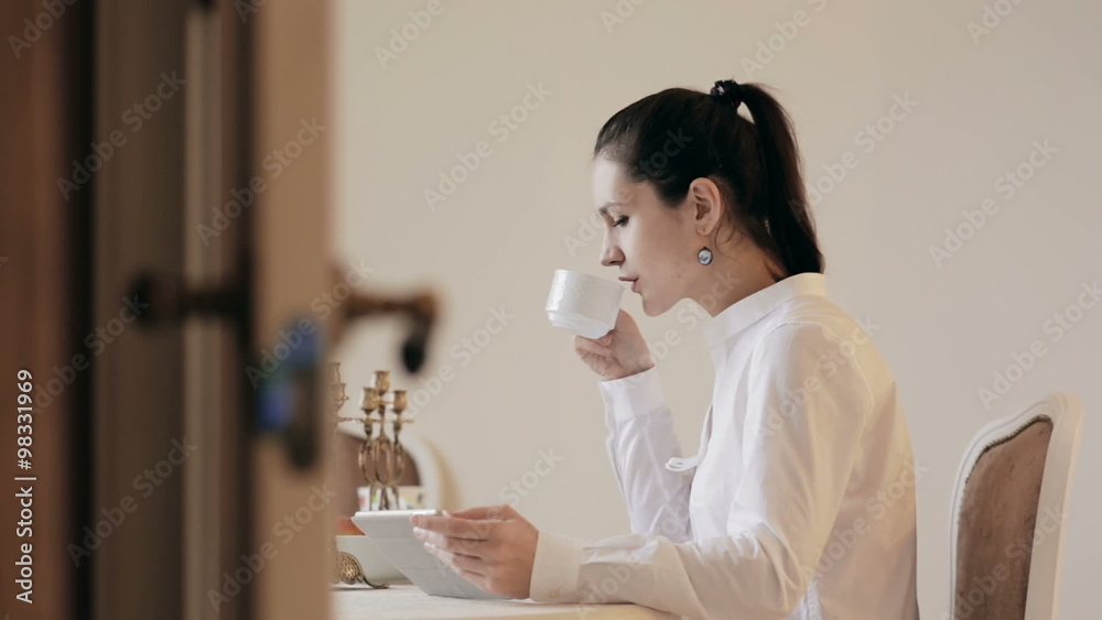 Woman using tablet and drinking coffee by table 