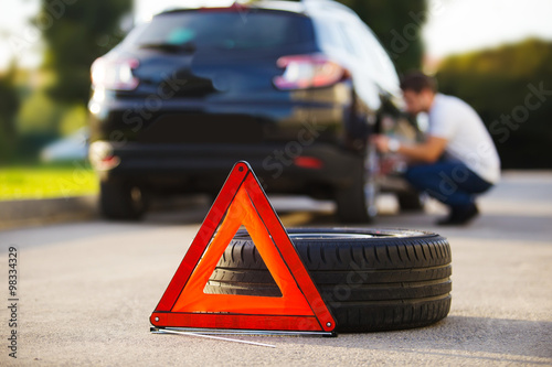 Sad and depressed man sitting near car with punctured tire