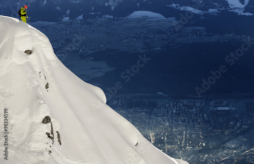 A freeride skier stands on the top of a mountain in powder snow on a sunny day in western Austria