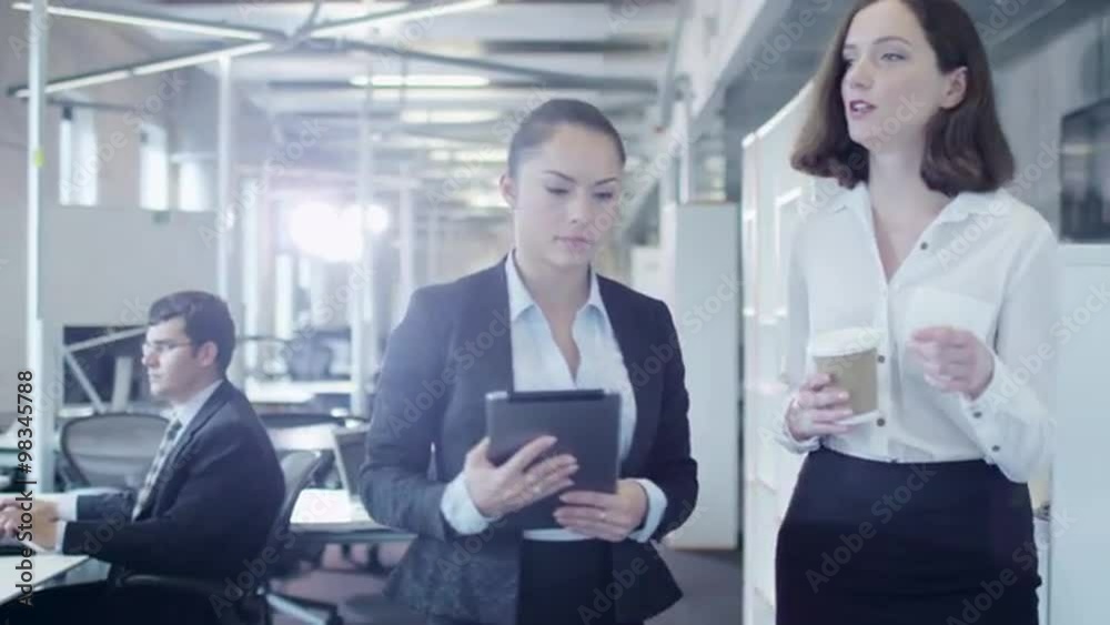 Two Attractive Female Workers are Walking through Office. One of them holding Tablet PC. Shot on RED Cinema Camera. Two Attractive Female Workers are Walking through Office. One of them holding Tablet PC. Shot on RED Cinema Camera.