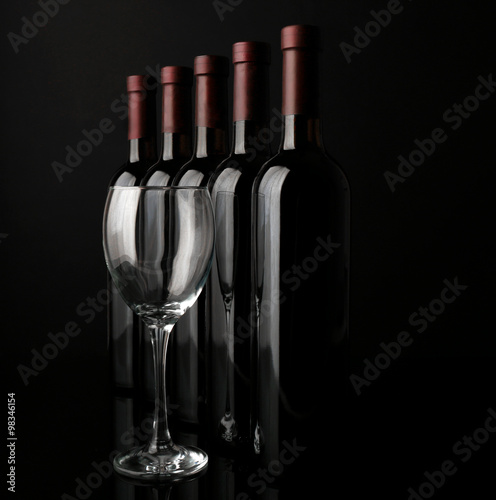 Glass and wine bottles in a row on black  background, close up