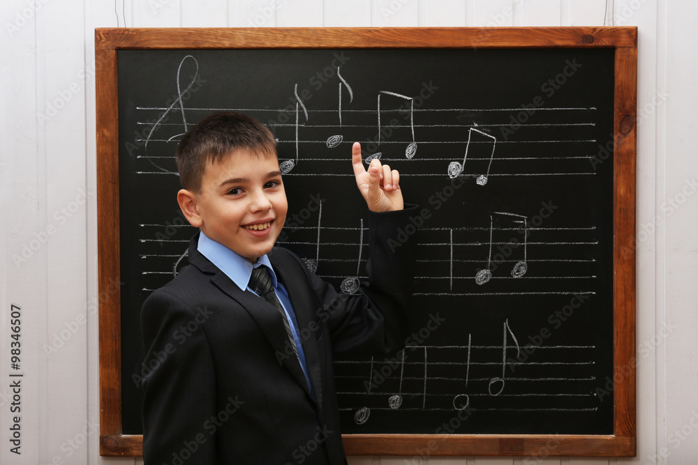 Young cute schoolboy standing at the blackboard with musical notes Young cute schoolboy standing at the blackboard with musical notes