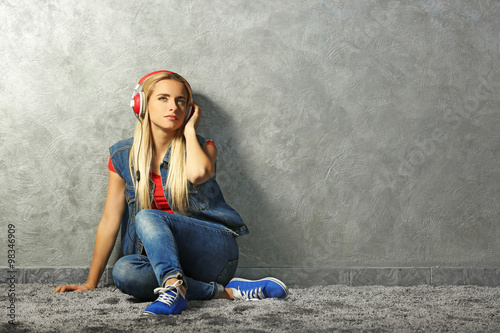 Young woman sitting on the floor and listening to music on a grey wall background