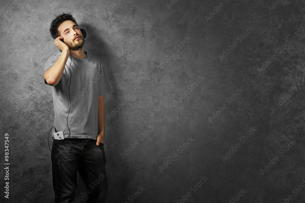 Young man listening music with headphones on grey wall background