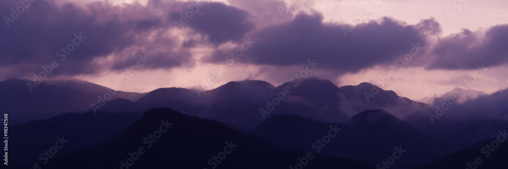 Silhouette of Mountains Above the Water under purple cloudscape clouds at sunset