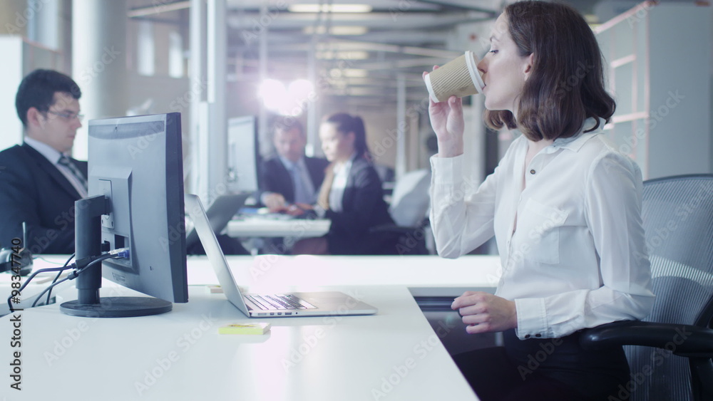 Female Office Worker is Working on Laptop and Drinking Coffee. Shot on RED Cinema Camera. Female Office Worker is Working on Laptop and Drinking Coffee. Shot on RED Cinema Camera.