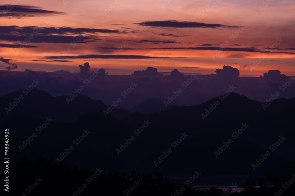 Silhouette of Mountains Above the Water under purple cloudscape clouds at sunset
