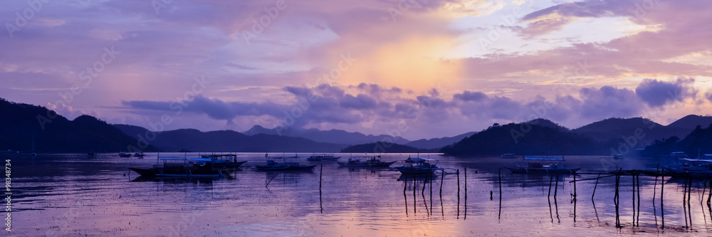 Pretty Pink orange Sky cloudscape over an island with reflection and wooden traditional filipino boats at Sunset on the Island of Coron