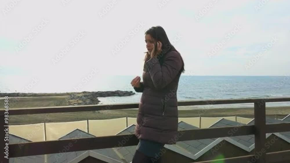 Beautiful brunette woman talking serious on the phone in front of the ocean Beautiful brunette woman talking serious on the phone in front of the ocean