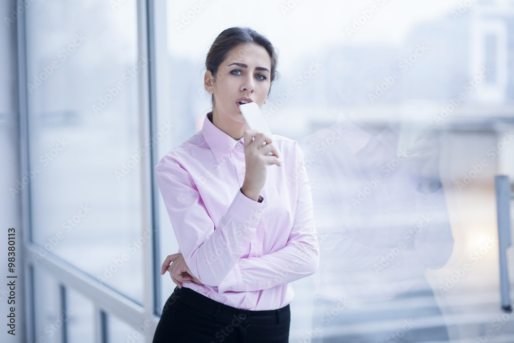 Businesswoman with cell phone standing next to the bright window Businesswoman with cell phone standing next to the bright window