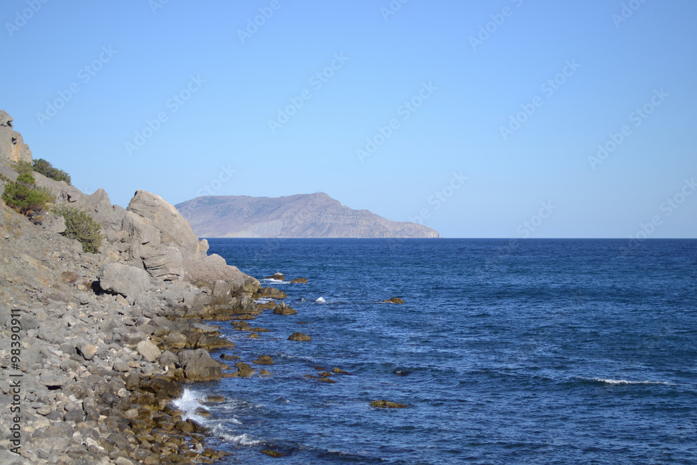View of an empty wild beach and mountains in the background of blue water and cloudless blue sky. A horizontal view. Noviy Svet, Crimea