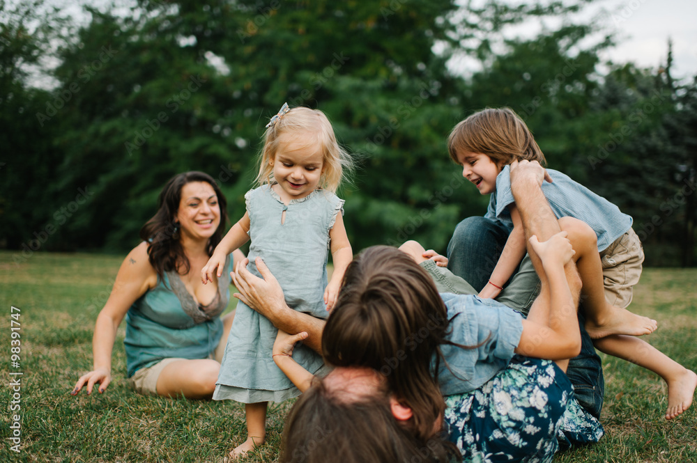 Happy young hipster family having fun while running, bowl,  rising up, piggyback ride their children in park on summer sunset
