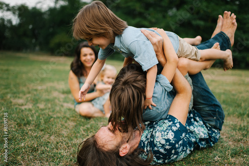 Happy young hipster family having fun while running, bowl,  rising up, piggyback ride their children in park on summer sunset
