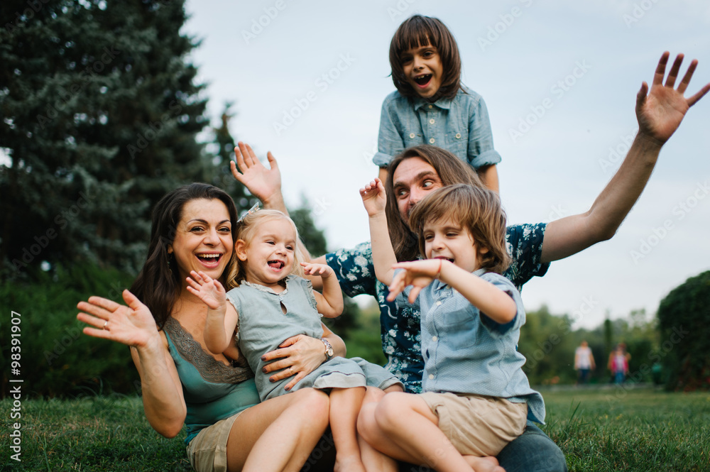 Happy young hipster family having fun, bowl,  rising up, piggyback ride their children in park on summer sunset
