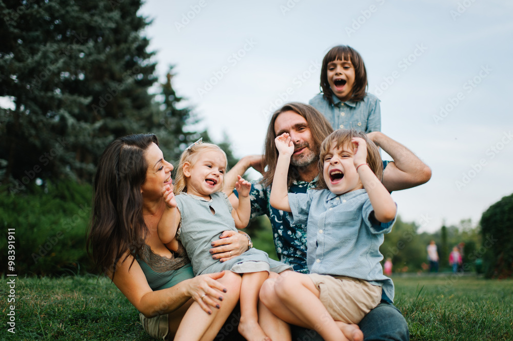 Happy young hipster family having fun, bowl,  rising up, piggyback ride their children in park on summer sunset
