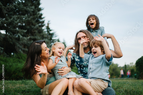 Happy young hipster family having fun, bowl, rising up, piggyback ride their children in park on summer sunset 