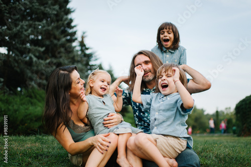Happy young hipster family having fun, bowl,  rising up, piggyback ride their children in park on summer sunset
