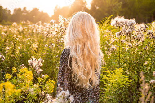 Fotografia Long haired blond woman turned back on sunset meadow
