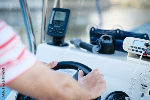 Hands at the steering wheel of a fishing boat with fish finder, GPS , compass and VHF radio