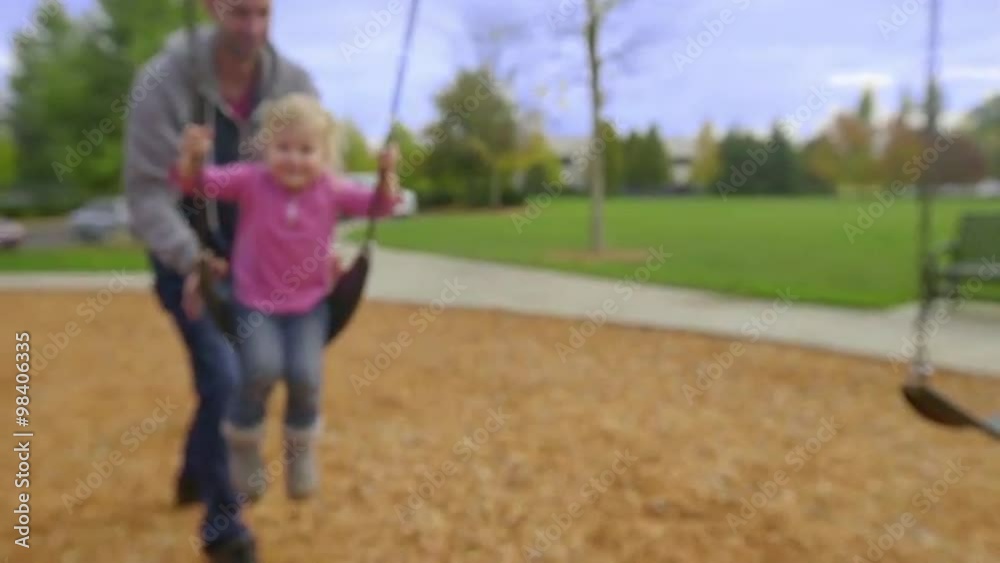 Father pushes his daughter on a swing as she smiles for the camera Father pushes his daughter on a swing as she smiles for the camera