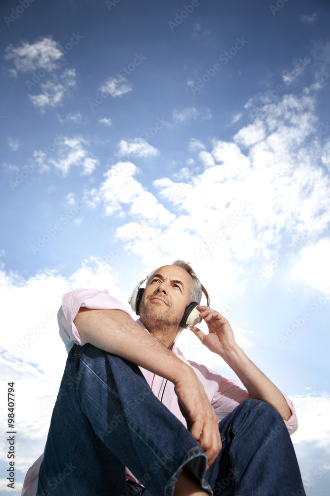 Portrait of man hearing music with headphones in front of clouded sky Portrait of man hearing music with headphones in front of clouded sky