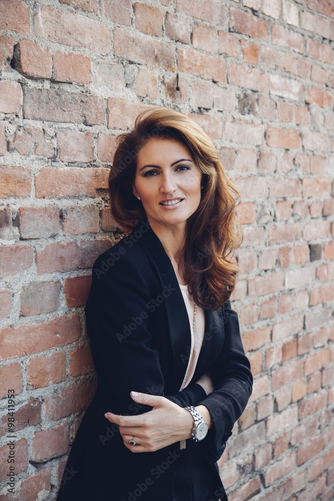 Portrait of smiling businesswoman leaning against brick wall