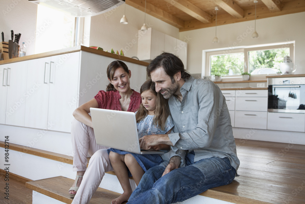 Happy family sitting on kitchen steps, daughter using laptop Happy family sitting on kitchen steps, daughter using laptop
