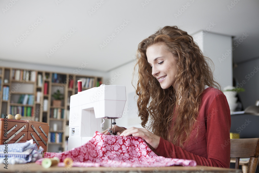 Smiling woman at home using sewing machine Smiling woman at home using sewing machine