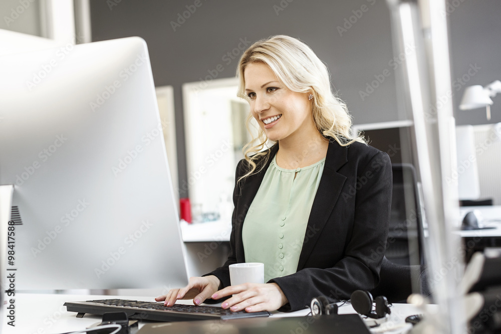 Smiling blond woman working at desk in office Smiling blond woman working at desk in office