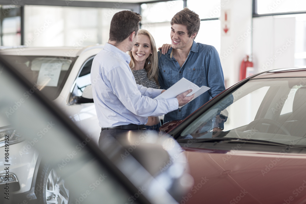 Car dealer showing brochure to young couple in showroom Car dealer showing brochure to young couple in showroom