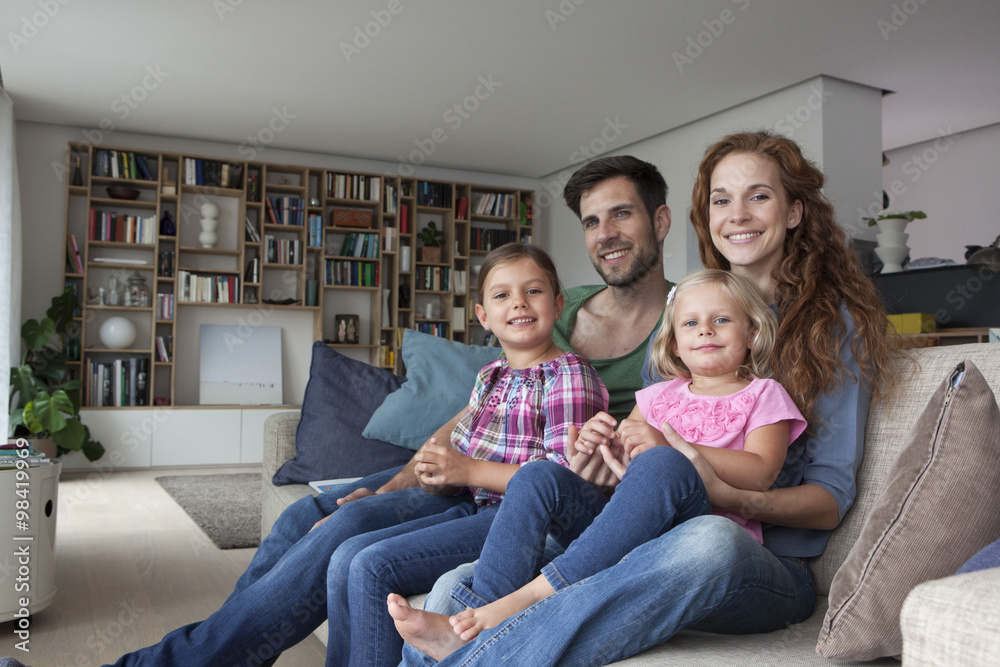 Family portrait of couple with two little girls sitting together on couch in the living room Family portrait of couple with two little girls sitting together on couch in the living room