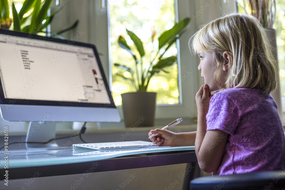 © Westend61 - Little girl looking at computer monitor at home