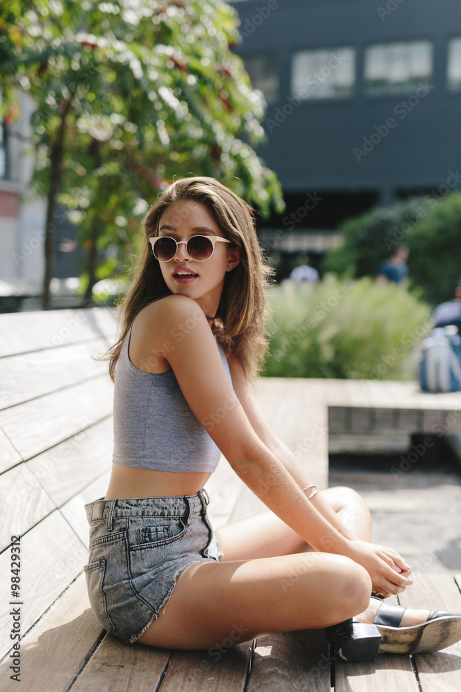 Brunette young woman wearing sunglasses relaxing on bench Brunette young woman wearing sunglasses relaxing on bench