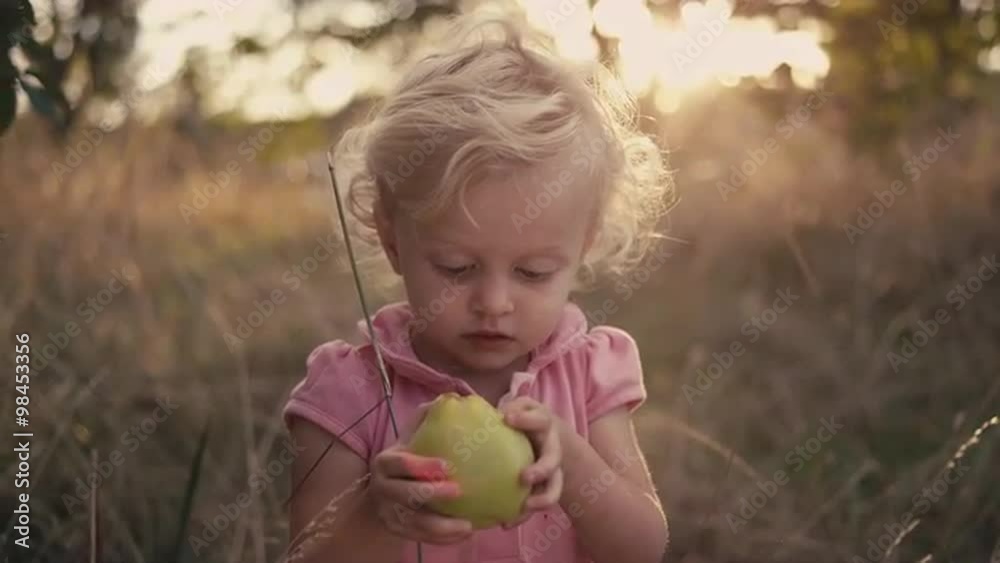 A cute little girl in a field holding an apple that she just picked, with lens flare A cute little girl in a field holding an apple that she just picked, with lens flare