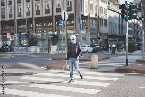 Young handsome caucasian man walking through pedestrian crossing, wearing an alien mask - surreal, eccentri concept