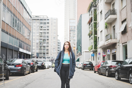 Knee figure of young handsome caucasian reddish straight hair woman posing on the middle of the street, hands in pocket, loooking upward, pensive - thoughtful, thinking future concept © Eugenio Marongiu