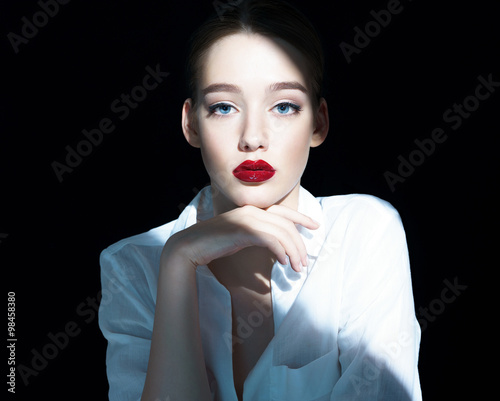 фотографія Portrait of a beautiful sensual brunette girl with red lips / close-up of an attractive girl of the European appearance in a white shirt, photography on a dark background