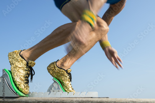 Athlete wearing gold running shoes takes off in a blur from from the race track starting blocks 